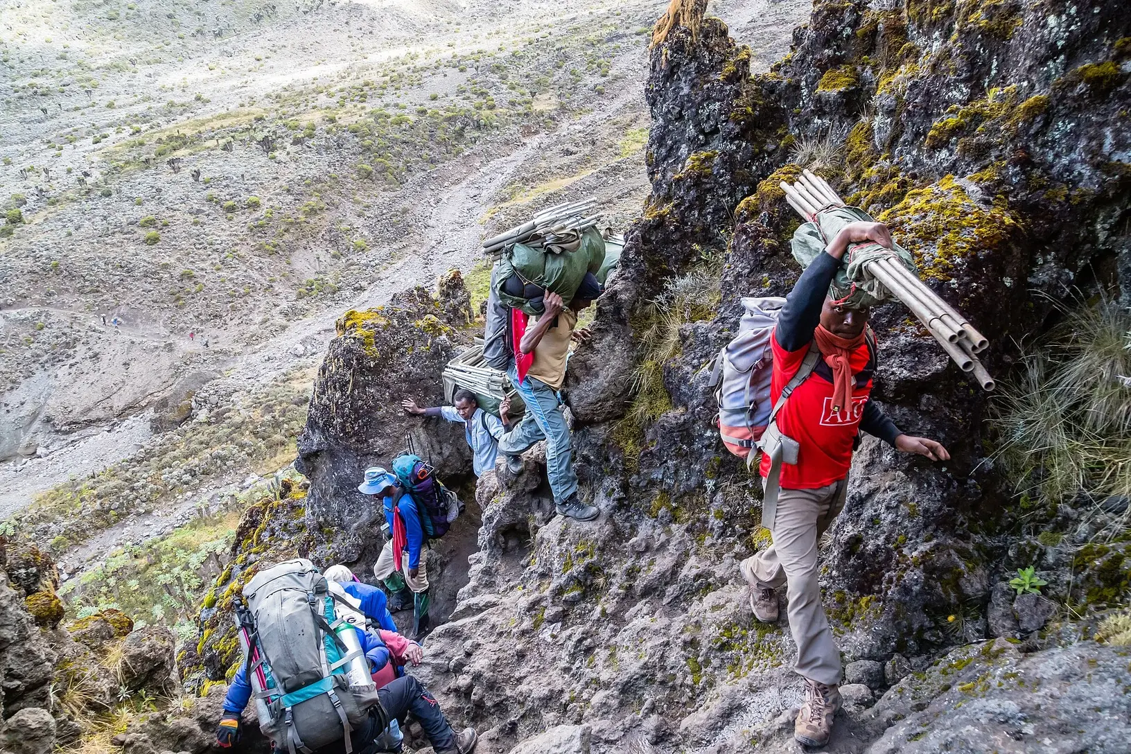 Several hikers and porters carrying equipment while climbing the Barranco Wall on Kilimanjaro.