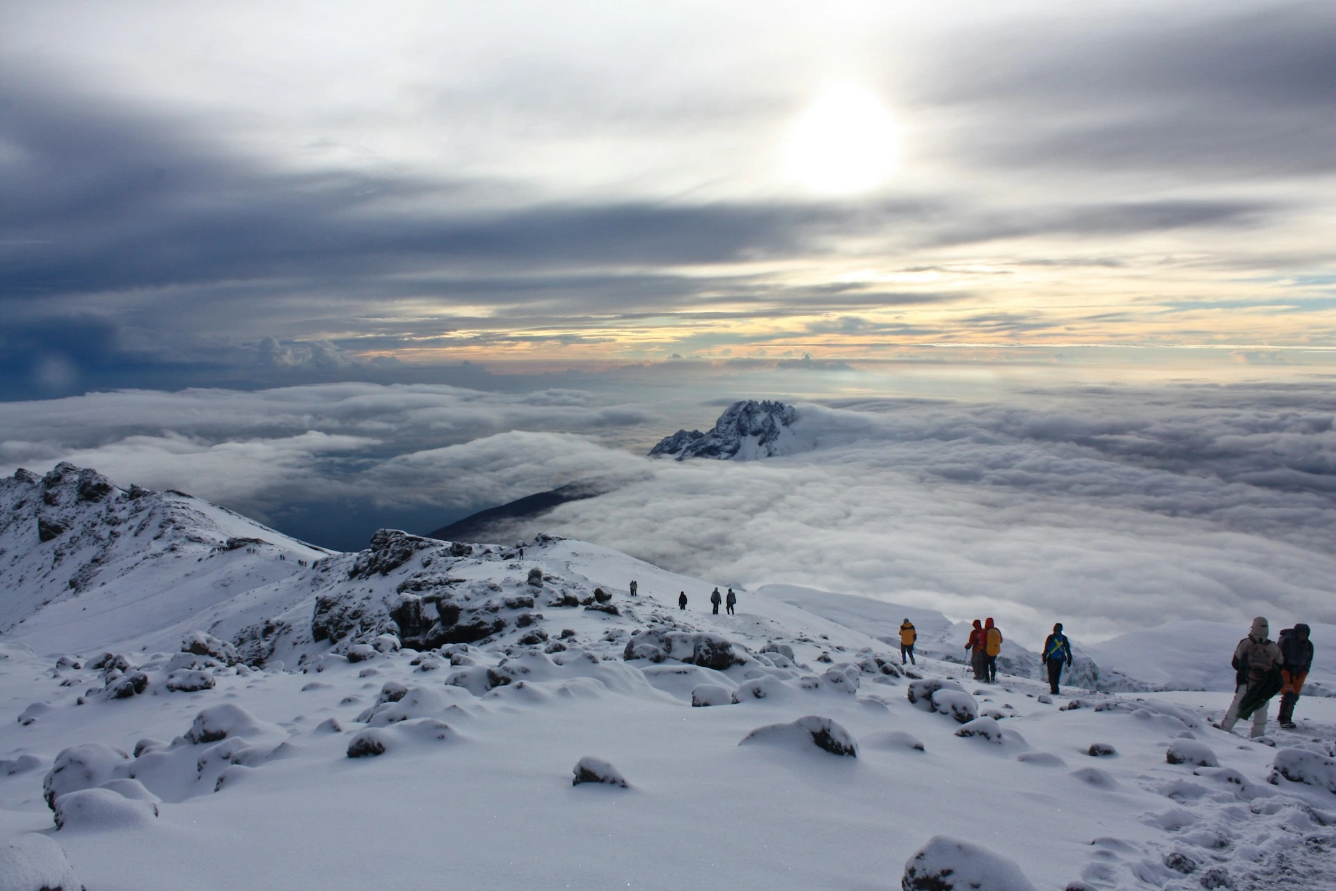 Several hikers above the clouds surrounded by snow near Uhuru Peak.
