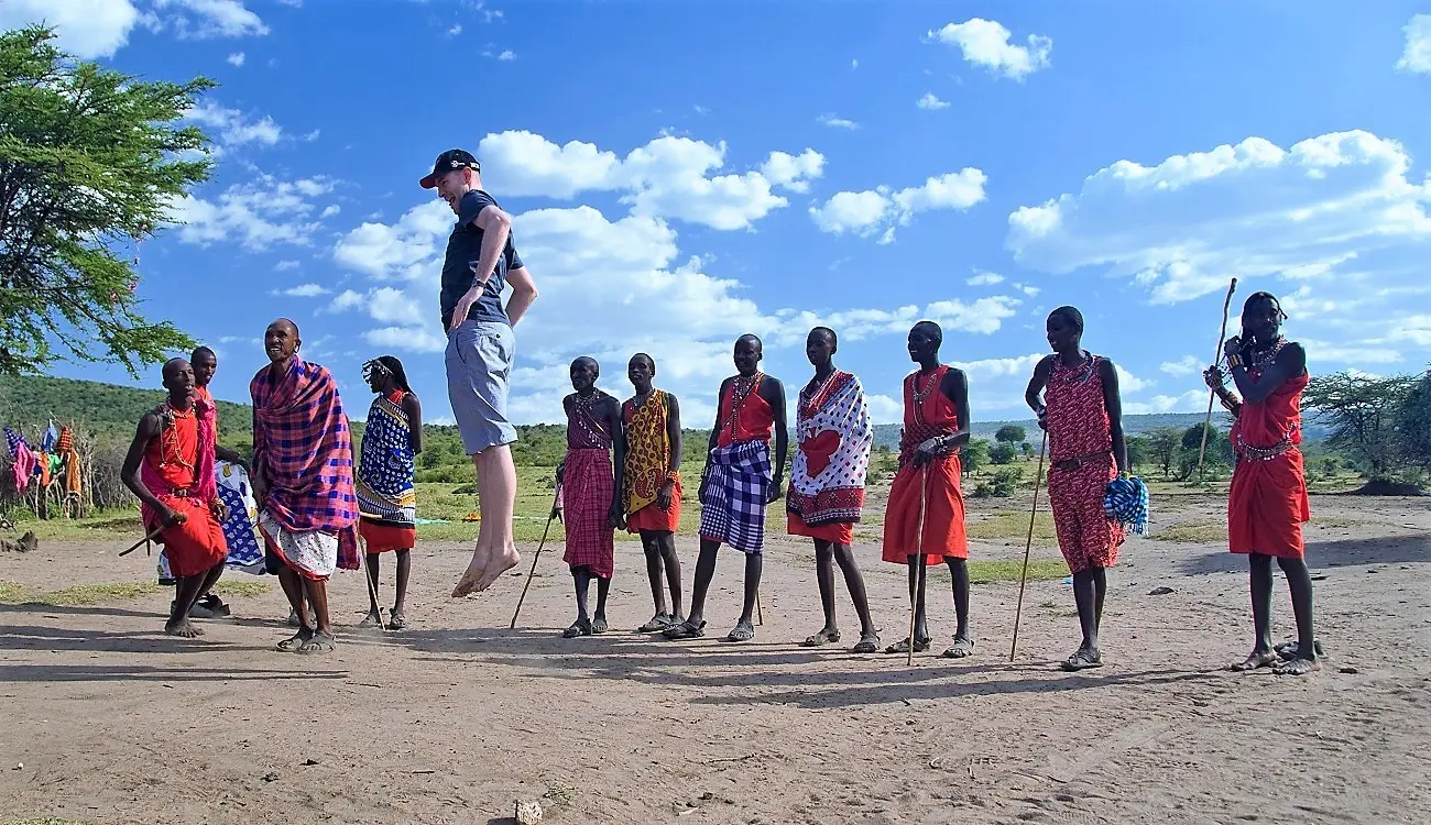 A group of Maasai and a tourist perform the Maasai jumping dance. The tourist is in the middle of jumping.
