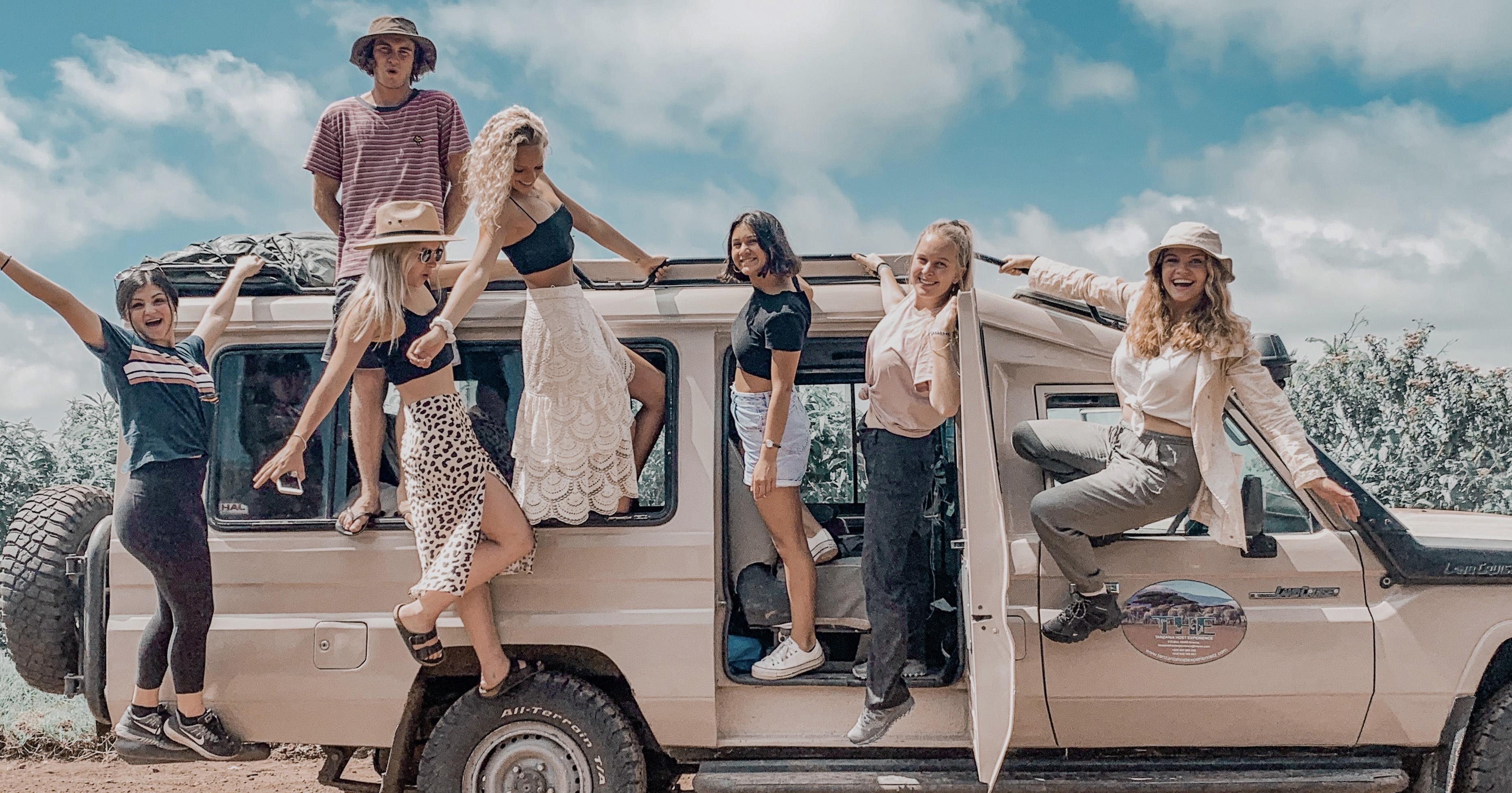 Seven tourists hanging out the doors and windows of a safari vechicle.