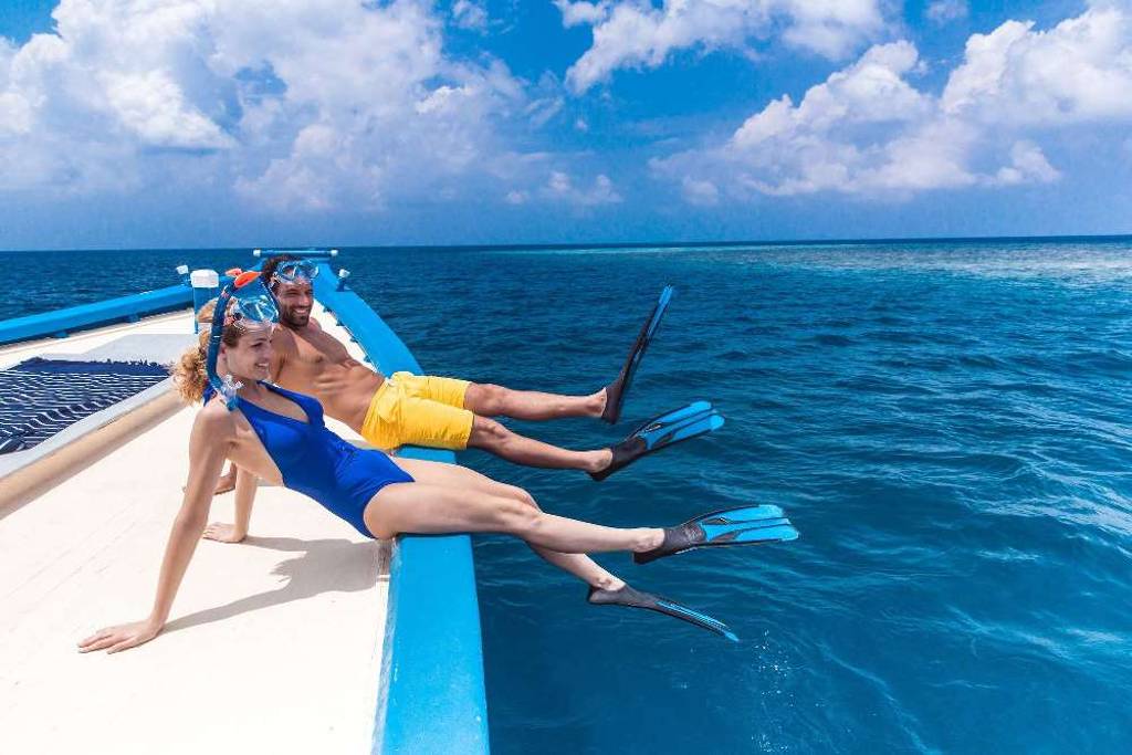 Two people in snorkel gear with their feet off the side of a boat.