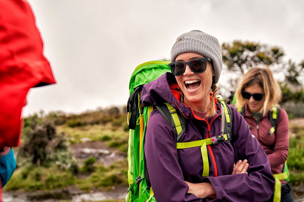 A woman laughing wearing full hiking gear on Kilimanjaro.